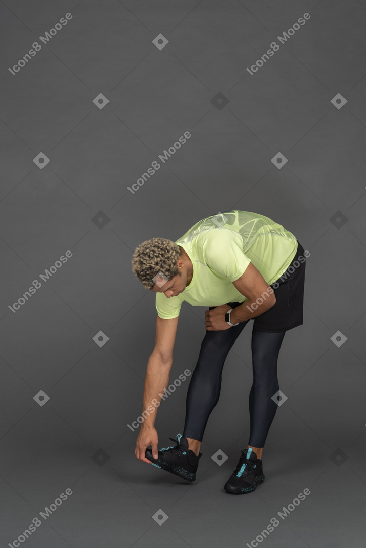 Hombre atlético agachándose y tocando sus zapatos para correr
