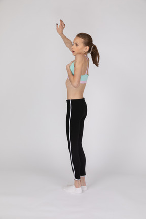 Vue latérale d'une adolescente surprise en tenue de sport mettant la main sur la poitrine et levant la main