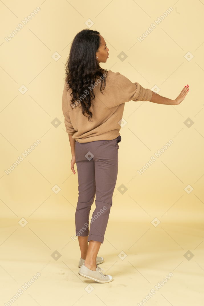Three-quarter back view of a dark-skinned young female outstretching hand