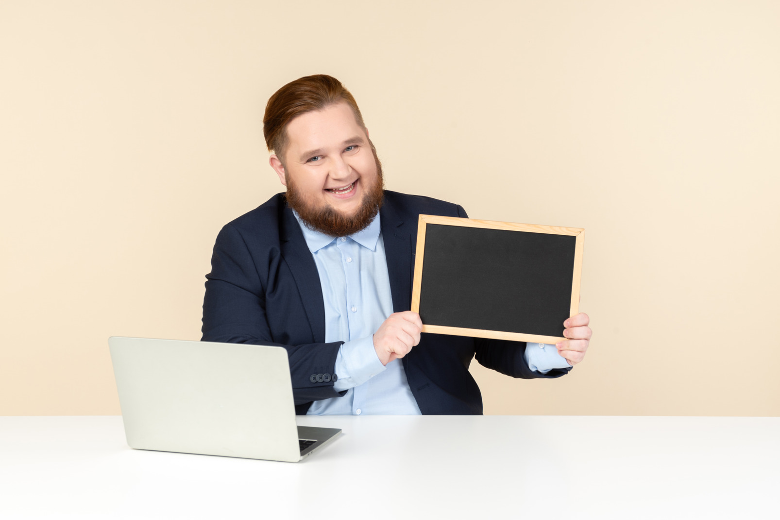 Laughing young man sitting at the desk and holding a blackboard