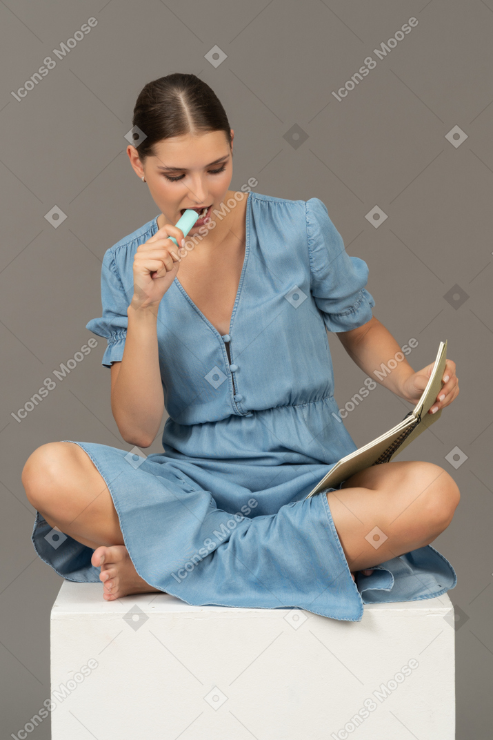 Vista frontale della giovane donna seduta su un cubo con pennarello e taccuino