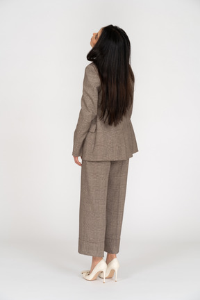 Three-quarter back view of a young lady in brown business suit throwing head back