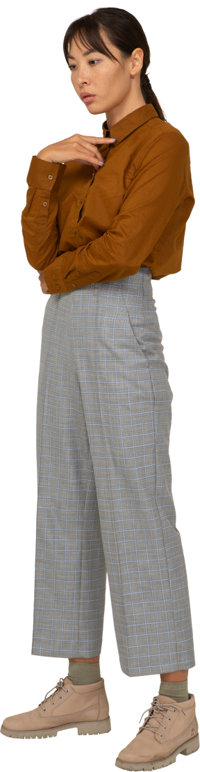 Vista di tre quarti di una giovane donna asiatica premurosa in calzoni e camicetta