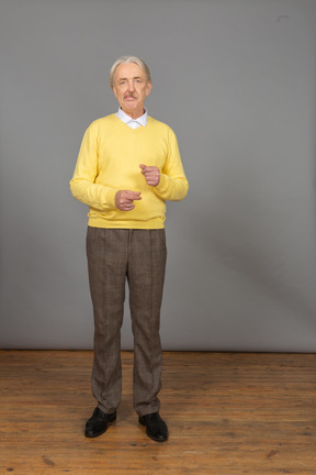 Vorderansicht eines alten grimassenmannes im gelben pullover, der hände hebt und kamera betrachtet