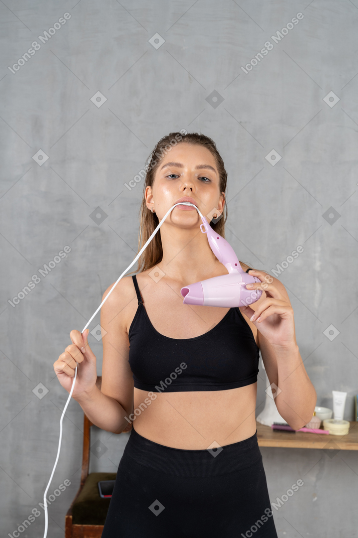 Front view of a young woman biting down on a hairdryer cord