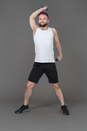 Expressive young man exercising with dumbbells