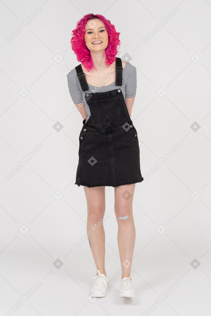 Garota sorridente de cabelo rosa posando com as mãos atrás das costas