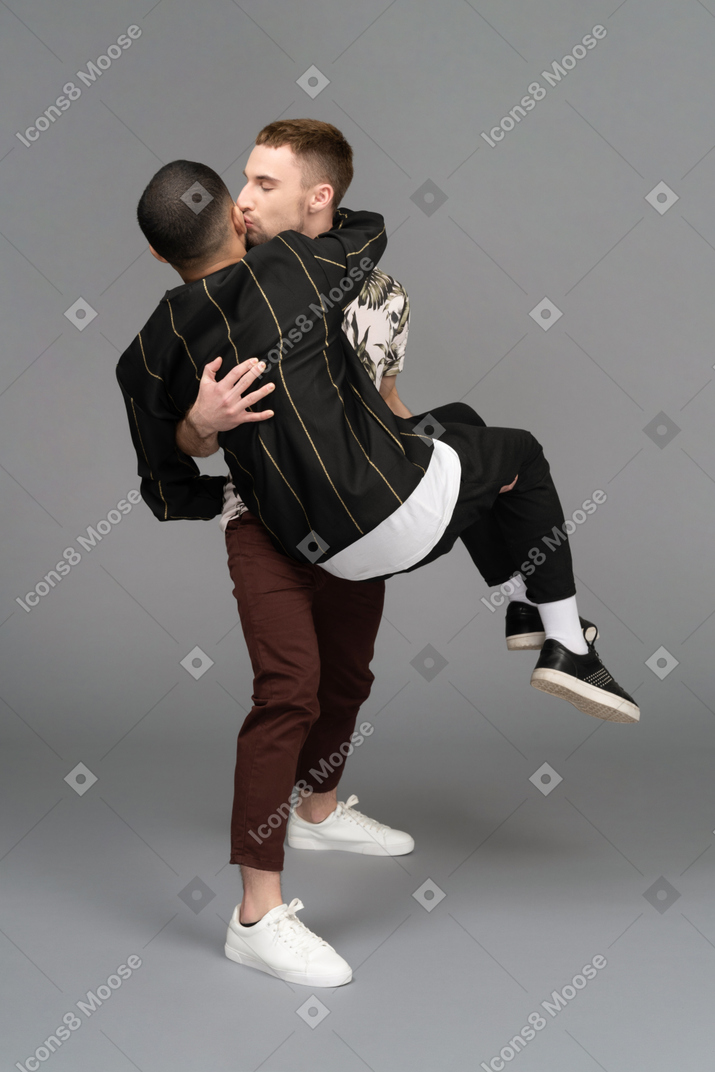 Молодой человек целует другого мужчину в щеку, держа его в свадебном стиле
