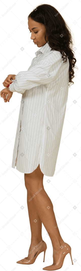 Vista laterale di una giovane femmina dalla carnagione scura in abito bianco che si abbottona la manica