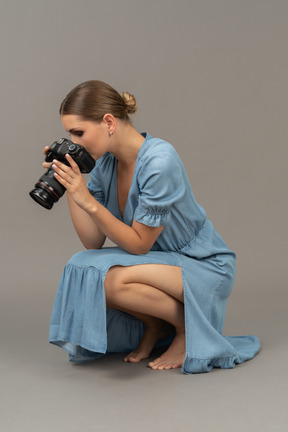 Dreiviertelansicht einer jungen frau in blauem kleid, die auf einem boden sitzt und eine aufnahme macht