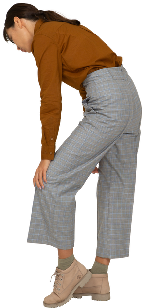 Vista traseira a três quartos de uma jovem mulher asiática de calça e blusa, inclinada para a frente