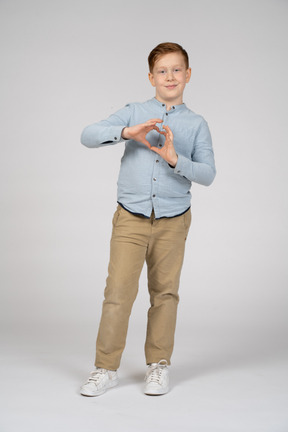 Vista frontal de um menino fazendo coração com os dedos e olhando para a câmera