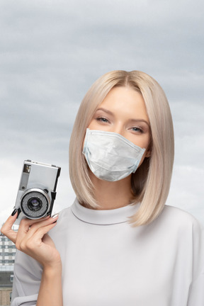 A woman wearing a face mask holding a camera