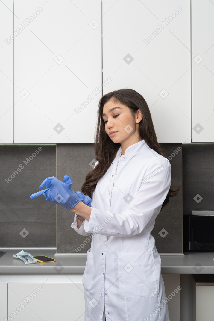 Three-quarter view of a young female doctor putting on protective gloves