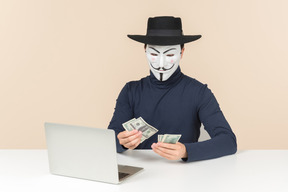 Hacker con máscara de vendetta contando dinero