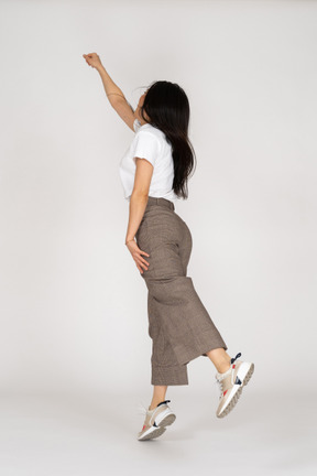 Three-quarter back view of a jumping young lady in breeches and t-shirt outstretching her hand