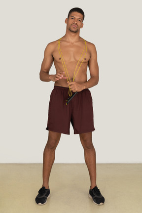 Bare chested young man in sport shorts standing with jumping rope over his neck