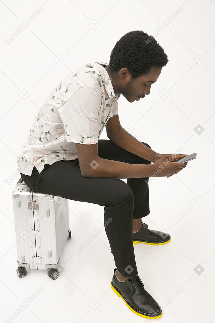 非洲裔人坐在行李上，并使用他的智能手机