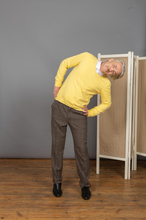 Front view of an old man putting hands on hips while leaning aside