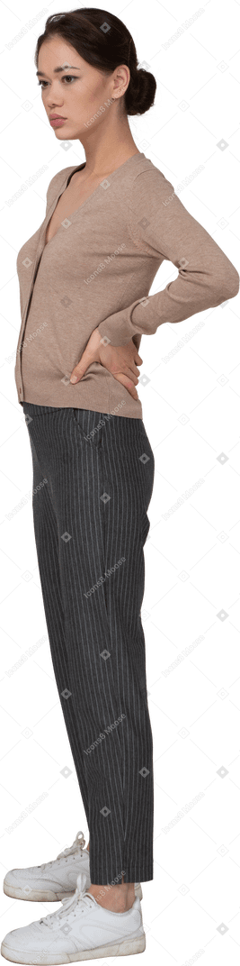 Vista di tre quarti di una giovane donna in pullover e pantaloni che mette le mani sui fianchi