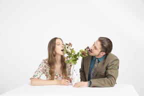 Pareja sentada en la mesa y comiendo moras de las ramas en el florero