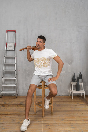 Vista frontal de un hombre en un taburete balanceando un ukelele furiosamente