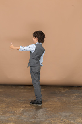 Vista laterale di un ragazzo in abito grigio che mostra il pollice in su