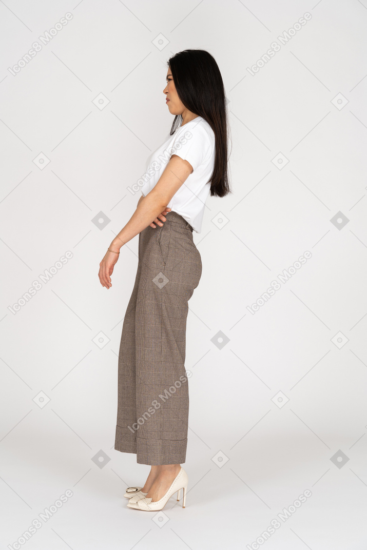 Vista laterale di una giovane donna con una smorfia scontenta in calzoni e maglietta