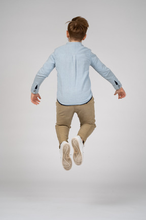 Back view of a boy in blue shirt and white sneakers jumping