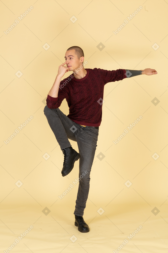 Vista frontale di un giovane uomo in equilibrio in pullover rosso toccandosi il naso