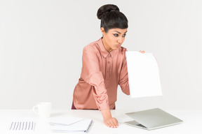 Displeased young indian office worker standing at the office desk and showing paper