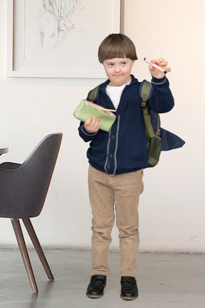 A young boy with backpack holding a pen