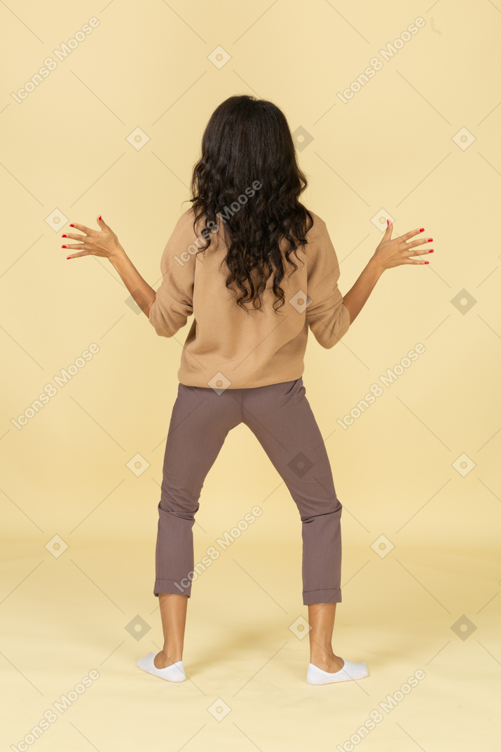 Back view of a funny dark-skinned young female outspreading her hands and legs