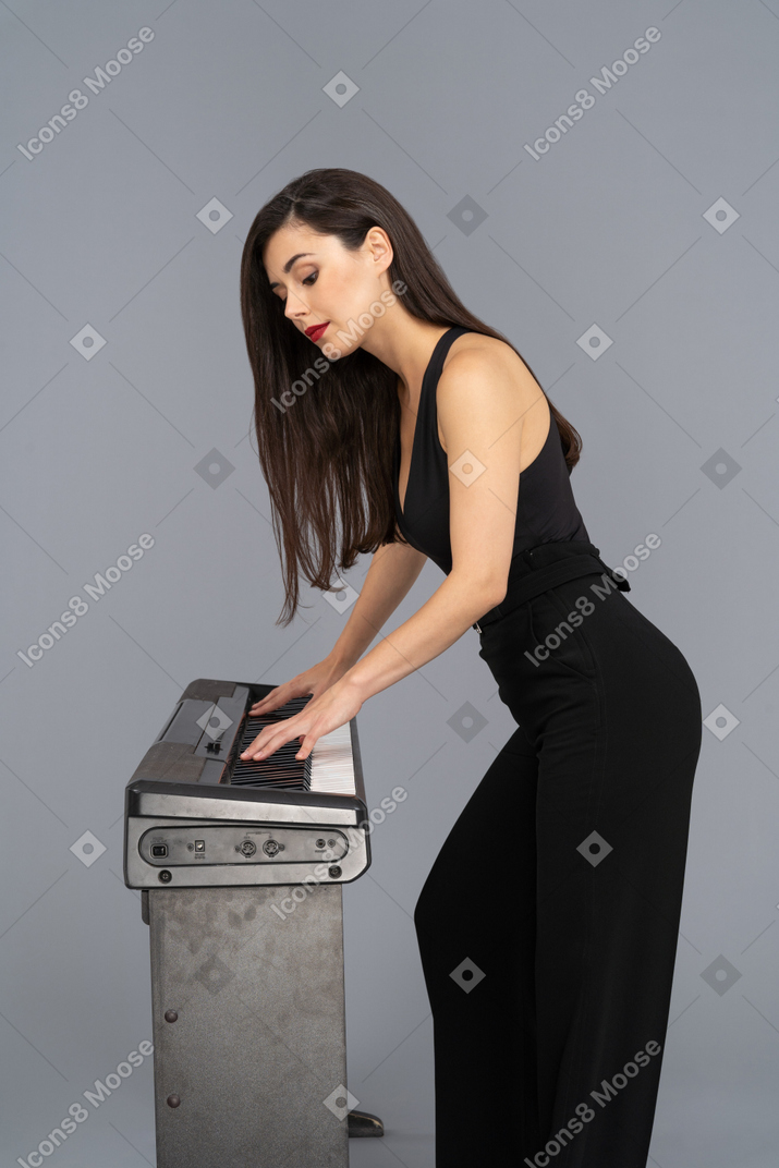 Jovem mulher tocando piano lateralmente para uma câmera