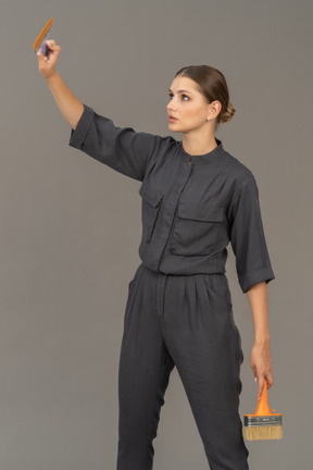Woman in gray coveralls posing with paint brushes