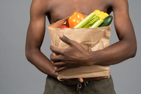 A shirtless young man holding a groceries bag