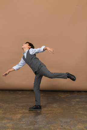 Side view of a boy in suit balancing on one leg with outstretched arms