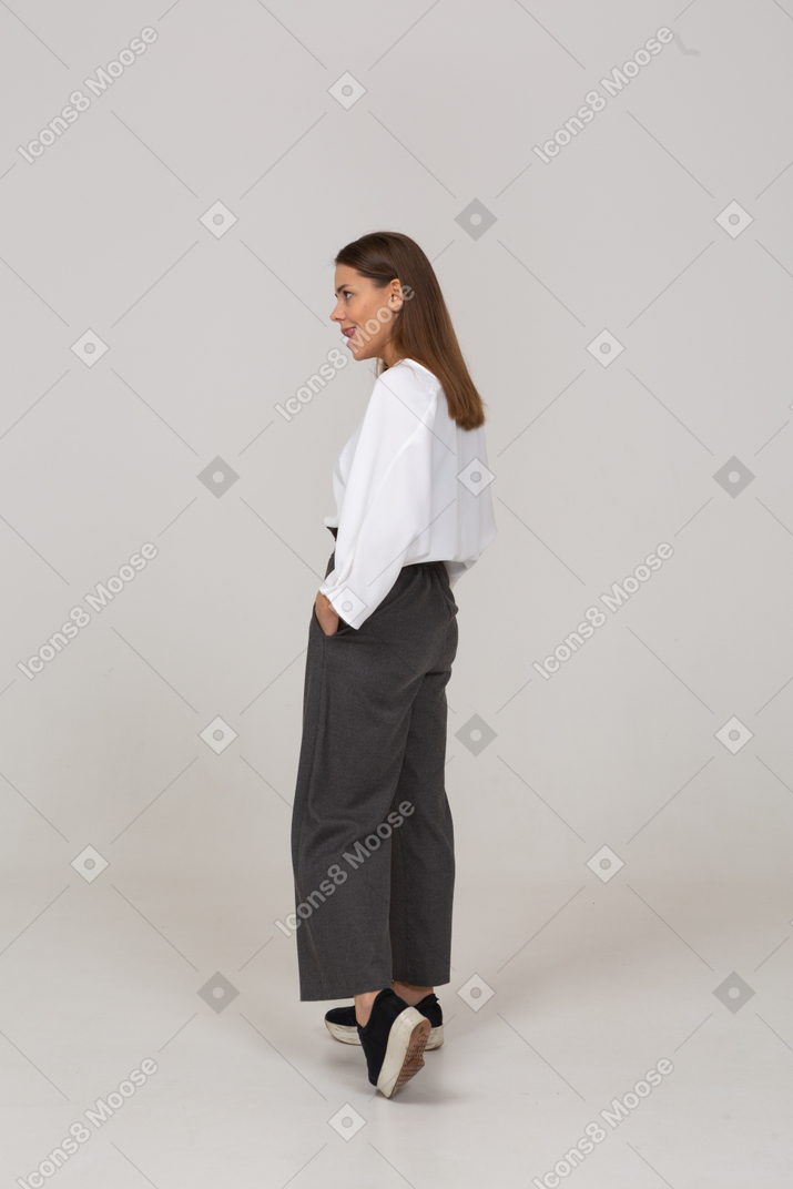 Vista posterior de tres cuartos de una joven en ropa de oficina mordiendo los labios mientras camina