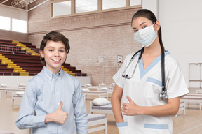 A boy and a nurse in scrubs giving thumbs up