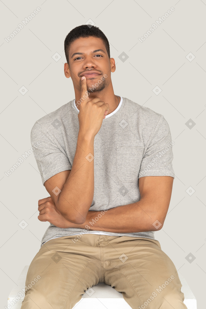 A good looking young man sitting on the white chair and holding his hand at the mouth