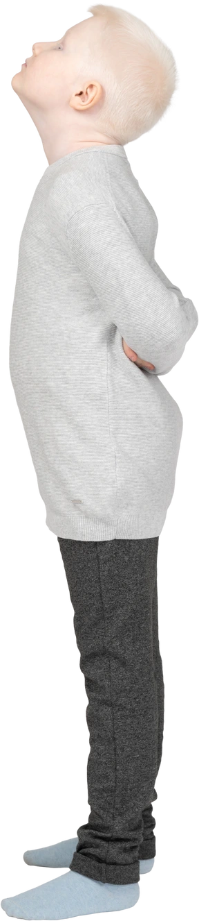 A blonde little boy in casual clothes standing and hiding hands behind