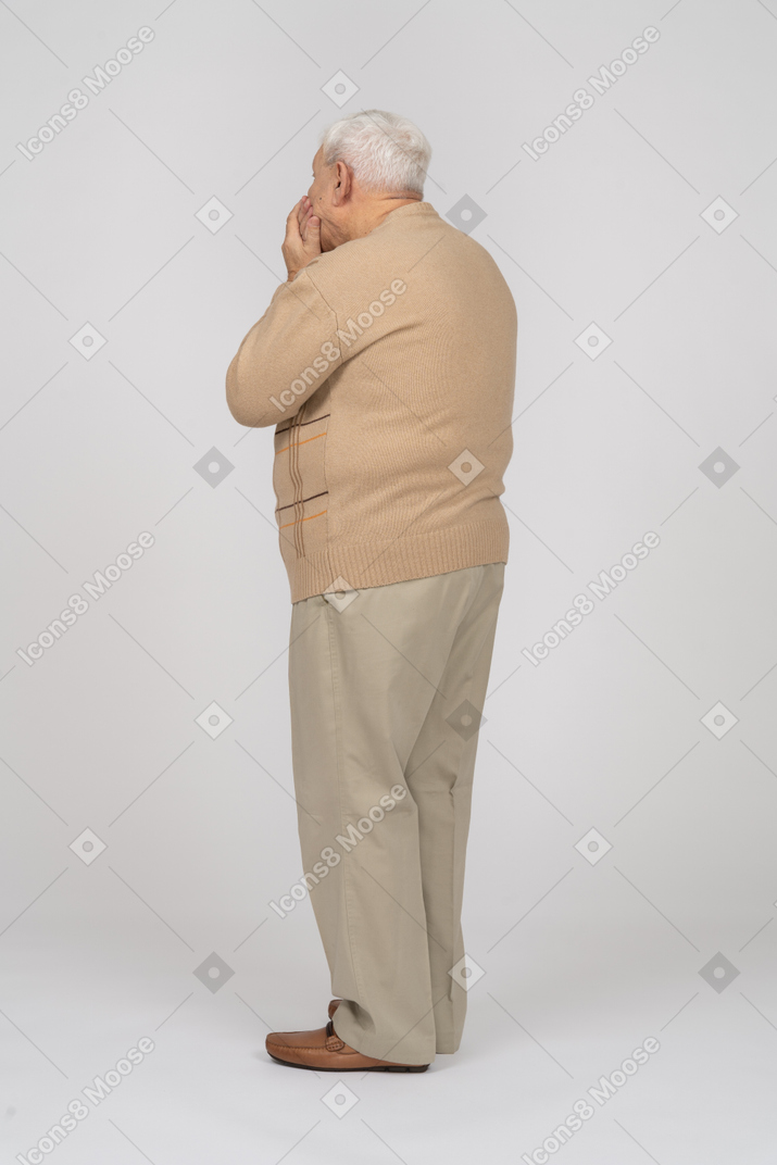 一位身穿休闲服的老人用手捂嘴的侧视图