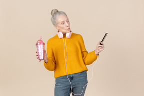 Mulher velha usando fones de ouvido e olhando no telefone