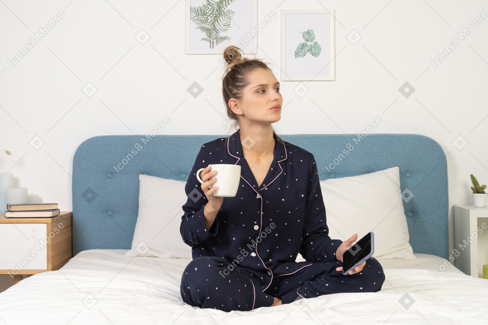 Frente a una mujer joven en pijama sentada en la cama sosteniendo la taza de café y teléfono móvil