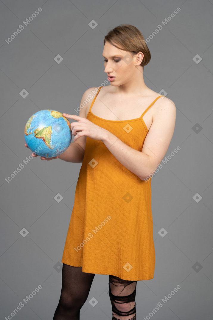 Jovem de vestido laranja apontando para algum lugar no globo