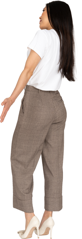 Vista posteriore di tre quarti di una giovane donna in calzoni e maglietta che allarga le mani