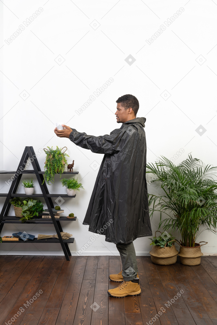 Vista lateral de um homem de capa de chuva segurando uma xícara