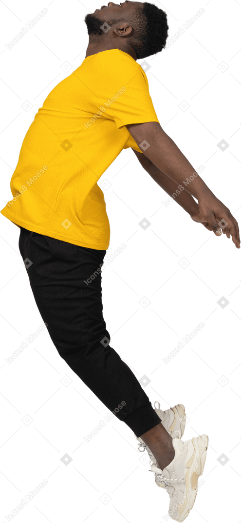 Vista lateral de um jovem de pele escura pulando em uma camiseta amarela estendendo as mãos