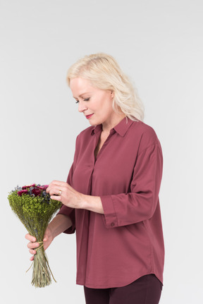 A nice-looking middle-aged blonde woman in a burgundy shirt and with a simple bouquet of flowers in her hands