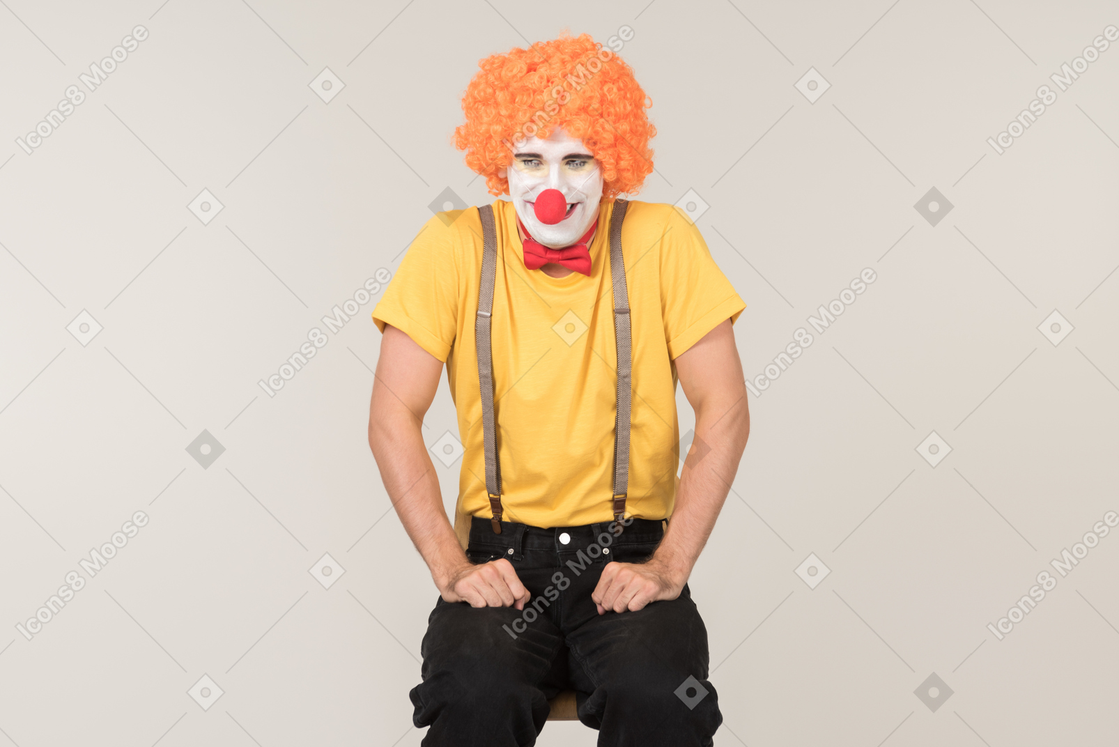 Male clown in red wig sitting on the chair